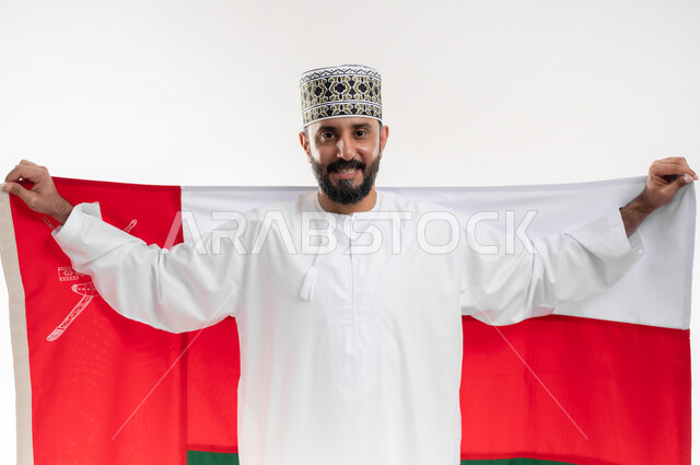 الفخر وإعتزاز بالهوية الوطنية، حب الوطن والانتماء إليه، إحياء ذكرى تأسيس الدولة 1775 م، العلم الوطني للبلاد، بورتريه  لرجل عربي خليجي عماني يرتدي الدشداشة و الكمة العمانية التقليدية يحتفل بذكرى اليوم الوطني العماني 18 نوفمبر، خلفية بيضاء