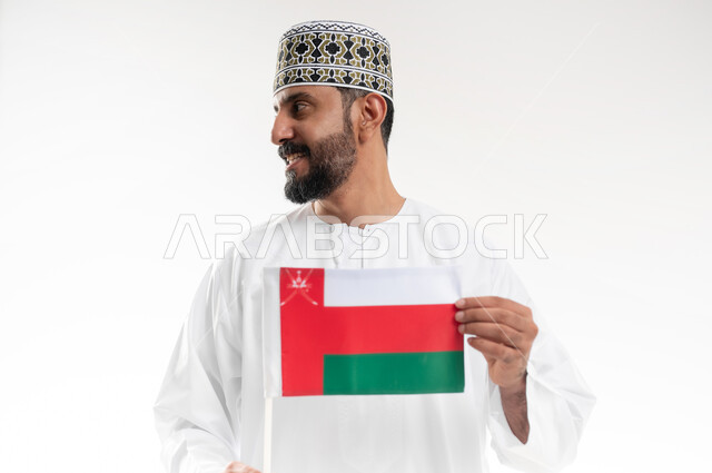 Pride and pride in national identity, love of country and belonging to it, commemorating the founding of the state in 1775 AD, the national flag of the country, portrait of an Arab Gulf Omani man wearing a dishdasha and the traditional Omani keffiyeh celebrating the anniversary of Omani National Day November 18, white background