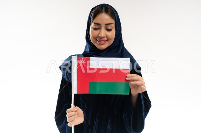 الفخر وإعتزاز بالهوية الوطنية، العلم الوطني للبلاد، بورتريه لإمرأة عربية خليجية عمانية محجبة ترتدي العباءة الملونة تحتفل بذكرى اليوم الوطني العماني 18 نوفمبر، رموز وثقافات وطنية , حب الوطن والانتماء إليه، إحياء ذكرى تأسيس الدولة 1775 م , خلفية بيضاء