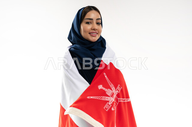الفخر وإعتزاز بالهوية الوطنية، العلم الوطني للبلاد، بورتريه لإمرأة عربية خليجية عمانية محجبة ترتدي العباءة الملونة تحتفل بذكرى اليوم الوطني العماني 18 نوفمبر، رموز وثقافات وطنية , حب الوطن والانتماء إليه، إحياء ذكرى تأسيس الدولة 1775 م , خلفية بيضاء