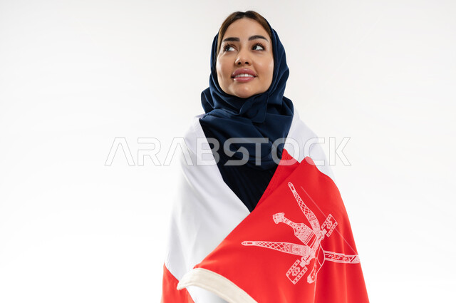 الفخر وإعتزاز بالهوية الوطنية، العلم الوطني للبلاد، بورتريه لإمرأة عربية خليجية عمانية محجبة ترتدي العباءة الملونة تحتفل بذكرى اليوم الوطني العماني 18 نوفمبر، رموز وثقافات وطنية , حب الوطن والانتماء إليه، إحياء ذكرى تأسيس الدولة 1775 م , خلفية بيضاء