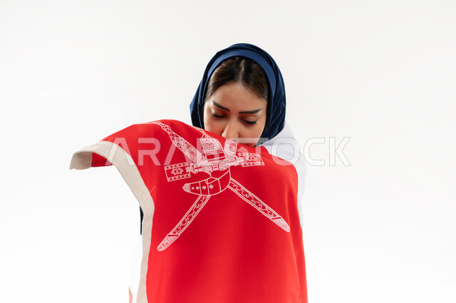 الفخر وإعتزاز بالهوية الوطنية، العلم الوطني للبلاد، بورتريه لإمرأة عربية خليجية عمانية محجبة ترتدي العباءة الملونة تحتفل بذكرى اليوم الوطني العماني 18 نوفمبر، رموز وثقافات وطنية , حب الوطن والانتماء إليه، إحياء ذكرى تأسيس الدولة 1775 م , خلفية بيضاء