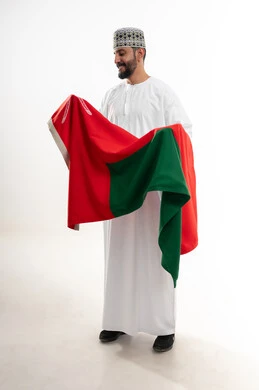 Commemorating the founding of the state in 1775 AD, national cultures and symbols, love of the homeland and belonging to it, the national flag of the country, a side portrait of an Arab Gulf Omani man wearing a dishdasha and the traditional Omani kummah celebrating the Omani National Day on November 18, full-length body, white background