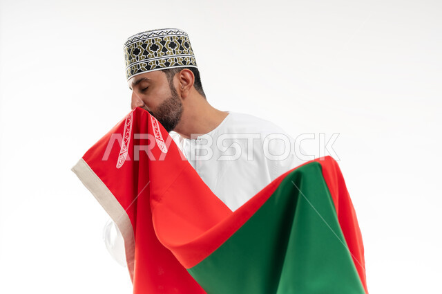 إحياء ذكرى تأسيس الدولة 1775 م، ثقافات و رموز وطنية , حب الوطن والانتماء إليه، العلم الوطني للبلاد، بورتريه من الجانب لرجل عربي خليجي عماني يرتدي الدشداشة و الكمة العمانية التقليدية يحتفل بذكرى اليوم الوطني العماني 18 نوفمبر، خلفية بيضاء