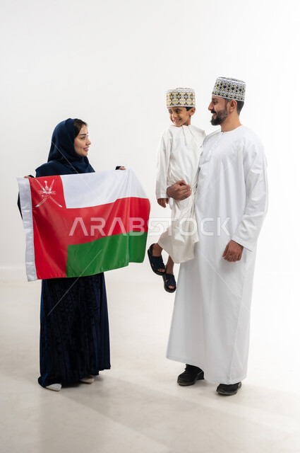 مناسبات واعياد وطنية, الفخر بإنجازات الوطن وثقافته, الاحتفال باليوم الوطني العماني 18 نوفمبر, إحياء ذكرى تأسيس الدولة 1775 م, بورتريه لرجل عربي خليجي عماني يرتدي الكمة والدشداشة يقف مع زوجته و ابنه يحتفلان بتوحيد السلطنة، الجسم بالطول الكامل، خلفية بيضاء