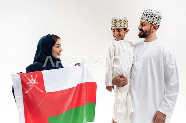 اعياد ومناسبات وطنية, الفخر بإنجازات الوطن وثقافته, الاحتفال باليوم الوطني العماني 18 نوفمبر, إحياء ذكرى تأسيس الدولة 1775 م, بورتريه لرجل عربي خليجي عماني يرتدي الكمة والدشداشة يقف مع زوجته و ابنه يحتفلان بتوحيد السلطنة، خلفية بيضاء