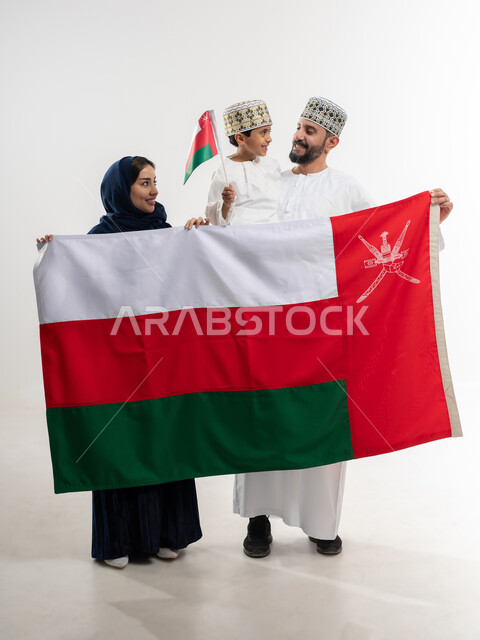 مناسبات واعياد وطنية, الفخر بإنجازات الوطن وثقافته, الاحتفال باليوم الوطني العماني 18 نوفمبر, إحياء ذكرى تأسيس الدولة 1775 م, بورتريه لرجل عربي خليجي عماني يرتدي الكمة والدشداشة يقف مع زوجته و ابنه يحتفلان بتوحيد السلطنة، الجسم بالطول الكامل، خلفية بيضاء