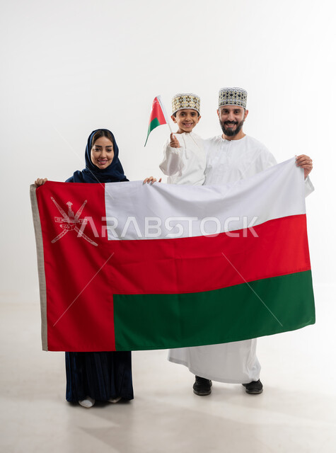 مناسبات واعياد وطنية, الفخر بإنجازات الوطن وثقافته, الاحتفال باليوم الوطني العماني 18 نوفمبر, إحياء ذكرى تأسيس الدولة 1775 م, بورتريه لرجل عربي خليجي عماني يرتدي الكمة والدشداشة يقف مع زوجته و ابنه يحتفلان بتوحيد السلطنة، الجسم بالطول الكامل، خلفية بيضاء