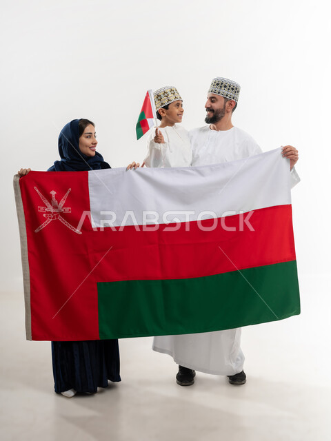 مناسبات واعياد وطنية, الفخر بإنجازات الوطن وثقافته, الاحتفال باليوم الوطني العماني 18 نوفمبر, إحياء ذكرى تأسيس الدولة 1775 م, بورتريه لرجل عربي خليجي عماني يرتدي الكمة والدشداشة يقف مع زوجته و ابنه يحتفلان بتوحيد السلطنة، الجسم بالطول الكامل، خلفية بيضاء