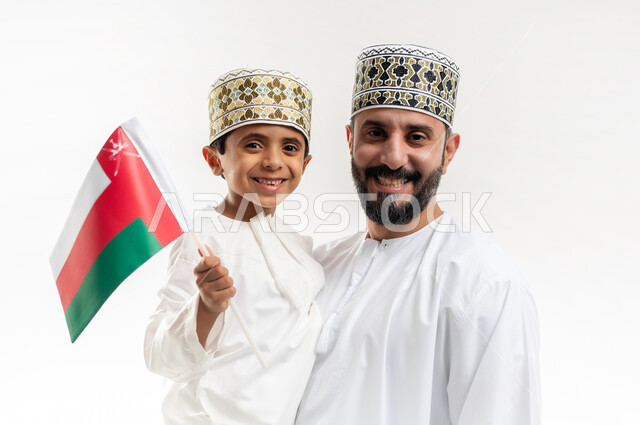إظهار مشاعر الاعتزاز بالوطن، الفخر بإنجازات الوطن وثقافته, الاحتفال باليوم الوطني العماني 18 نوفمبر, إحياء ذكرى تأسيس الدولة 1775 م, بورتريه لرجل عربي خليجي عماني يرتدي الكمة والدشداشة يقف مع ابنه يحتفلان بتوحيد السلطنة، خلفية بيضاء
