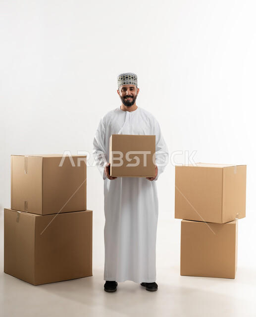 إستلام المشتريات و تسليم البضائع للزبائن, توصيل الطلبيات بالوقت المحدد و بشكل سليم, بورتريه لرجل عربي خليجي عماني يرتدي الكمه و الدشداشة يحمل بيده صندوق كرتوني مغلق, الجسم بالطول الكامل, خلفيه بيضاء