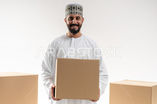 إستلام المشتريات و تسليم البضائع للزبائن, توصيل الطلبيات بالوقت المحدد و بشكل سليم, بورتريه لرجل عربي خليجي عماني يرتدي الكمه و الدشداشة يحمل بيده صندوق كرتوني مغلق, خلفيه بيضاء