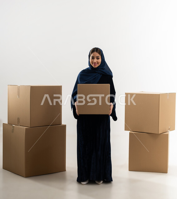 تسليم البضائع للزبائن وإستلام المشتريات, توصيل الطلبيات بالوقت المحدد و بشكل سليم, بورتريه لإمراة عربية خليجية عمانية ترتدي العباءة الملونة والحجاب تحمل بيدها صندوق كرتوني مغلق, الجسم بالطول الكامل، خلفيه بيضاء