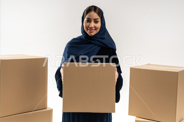 تسليم البضائع للزبائن وإستلام المشتريات, توصيل الطلبيات بالوقت المحدد و بشكل سليم, بورتريه لإمراة عربية خليجية عمانية ترتدي العباءة الملونة والحجاب تحمل بيدها صندوق كرتوني مغلق, خلفيه بيضاء