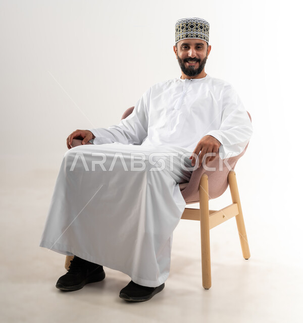 مفهوم الاسترخاء والاستمتاع بالأجواء الهادئة، بورتريه لرجل عربي خليجي عماني يرتدي الدشداشه والكمه يجلس على كرسي مريح، تعابير وإيماءات الراحة، خلفية بيضاء