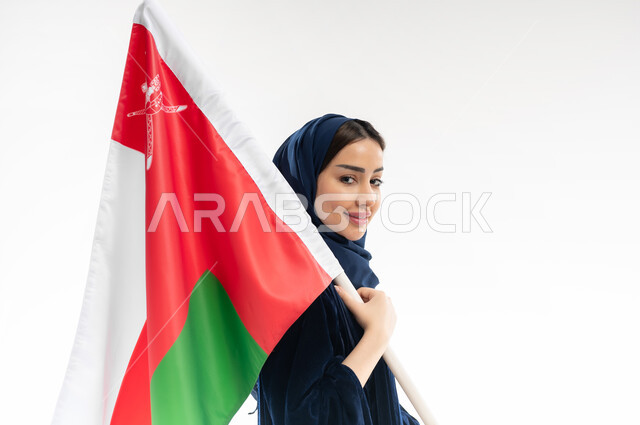 National symbols and cultures, love of the homeland and belonging to it, the national flag of the country, a portrait from the sides of a veiled Omani Gulf Arab woman wearing a colorful abaya celebrating the anniversary of the Omani National Day, November 18, commemorating the founding of the state in 1775 AD, white background