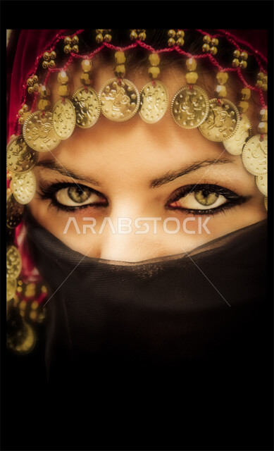 ابراز العيون المكحلة السوداء، مفهوم الحياء والستر، بورتريه مقرب لوجه امراه عربية سعودية خليجيه محجبه تقوم بوضع اللثام على وجهها، نظرات الأنوثه الناعمه، النظر الى الكاميرا