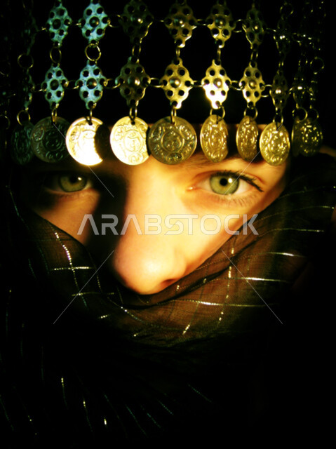 Highlighting the black kohl-lined eyes, the concept of modesty and concealment, a close-up portrait of the face of a veiled Saudi Arabian Gulf woman putting the niqab on her face, soft feminine looks, looking at the camera