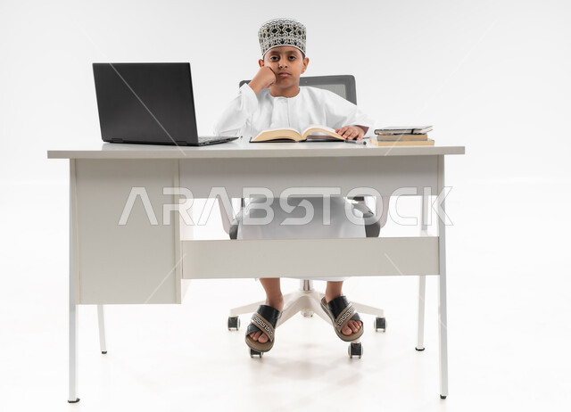 هدر وضياع الوقت، اللهو أثناء الدراسة، سلبيات التعلم عن بعد، تعابير التعب والإرهاق، استخدام التقنيات الحديثة، متابعة الحصص و حل الواجبات، بورتريه لصبي عربي خليجي عماني يرتدي الدشداشة والكمة يقوم بإهمال دروسه، صورة لكامل الجسم، خلفية بيضاء