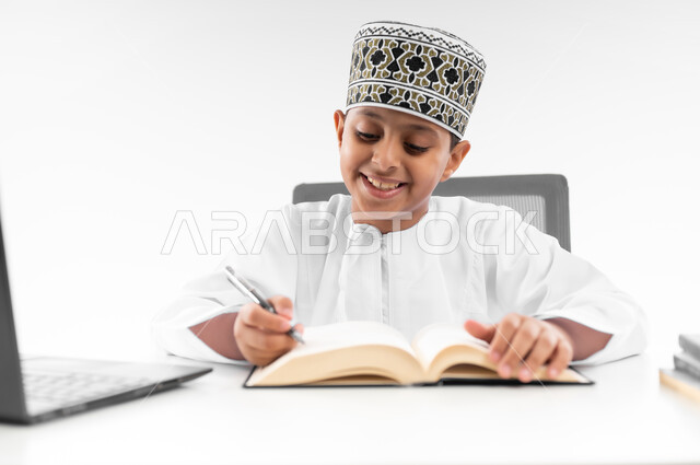 Following new educational methods, home e-learning, advanced schools and academies, modern technology and technology, close-up portrait of an Arab Gulf Omani boy wearing a dishdasha and a turban reviewing lessons using a laptop, white background
