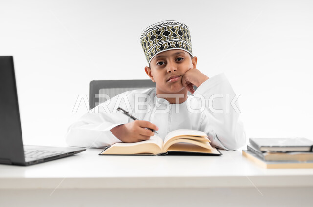 Having fun while studying, wasting time, disadvantages of distance learning, expressions of fatigue and exhaustion, using modern technologies, following up on classes and solving homework, close-up portrait of an Arab Gulf Omani boy wearing a dishdasha and a kimono neglecting his lessons, white background