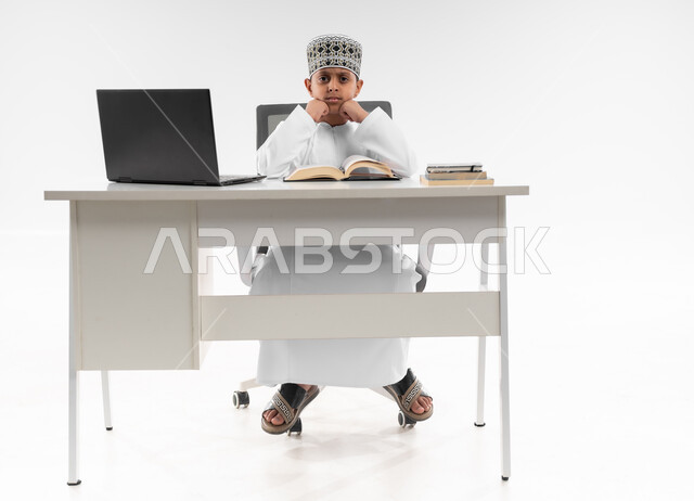 تعابير التعب والإرهاق، هدر وضياع الوقت، اللهو أثناء الدراسة، سلبيات التعلم عن بعد، استخدام التقنيات الحديثة، متابعة الحصص و حل الواجبات، بورتريه لصبي عربي خليجي عماني يرتدي الدشداشة والكمة يقوم بإهمال دروسه، صورة لكامل الجسم، خلفية بيضاء