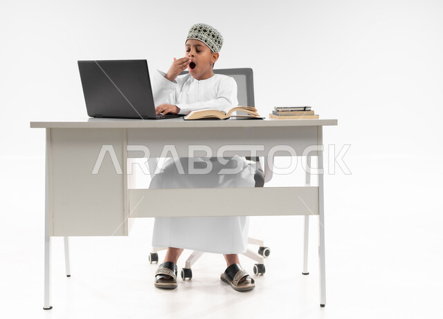 سلبيات التعلم عن بعد، تعابير النعاس والتعب والإرهاق، النوم على طاولة الدراسة، هدر وضياع الوقت، استخدام التقنيات الحديثة، بورتريه لصبي عربي خليجي عماني  يرتدي الدشداشة والكمة يضع يده على فمه بايماءات التثاؤب يقوم بإهمال دروسها، صورة لكامل الجسم، خلفية بيضاء