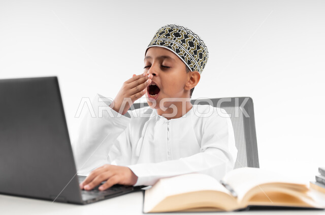 هدر وضياع الوقت، سلبيات التعلم عن بعد، تعابير النعاس والتعب والإرهاق، النوم على طاولة الدراسة، استخدام التقنيات الحديثة، بورتريه مقرب لصبي عربي خليجي عماني  يرتدي الدشداشة والكمة يضع يده على فمه بايماءات التثاؤب يقوم بإهمال دروسها، خلفية بيضاء
