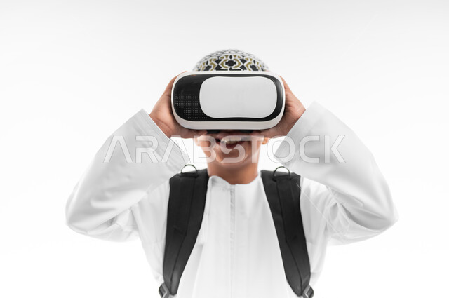 اتباع طرق تعليمية جديدة، مدارس وأكاديميات متطوره، بورتريه مقرب لتلميذ عربي خليجي عماني يرتدي الدشداشة والكمة يحمل الحقيبة المدرسية يضع نظارات الواقع الافتراضي، جمع التعلم مع الترفيه، إستخدام التقنيه والتكنولوجيا الحديثه، خلفيه بيضاء