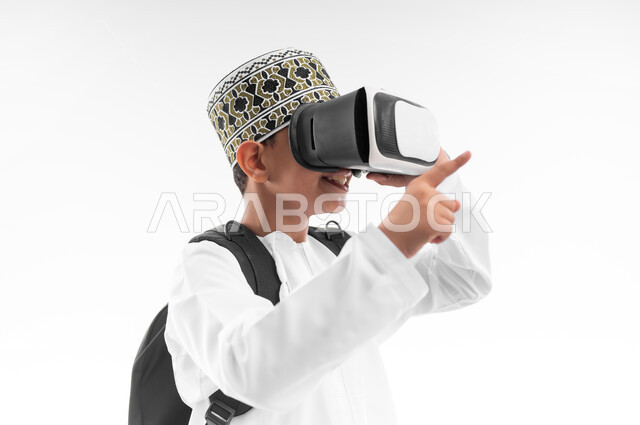 جمع التعلم مع الترفيه، مدارس وأكاديميات متطوره، اتباع طرق تعليمية جديدة، بورتريه مقرب من الجانب لتلميذ عربي خليجي عماني يرتدي الدشداشة والكمة يحمل الحقيبة المدرسية والكتاب يضع نظارات الواقع الافتراضي يشير لمكان ما، استخدام التقنيه والتكنولوجيا الحديثه، خلفيه بيضاء