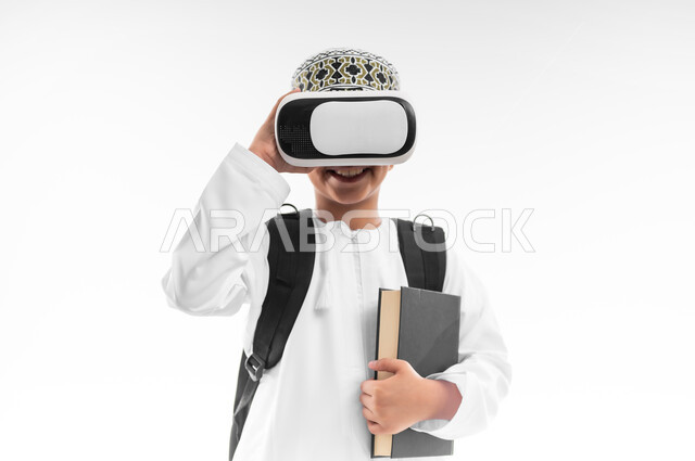 اتباع طرق تعليمية جديدة، مدارس وأكاديميات متطوره، بورتريه مقرب لتلميذ عربي خليجي عماني يرتدي الدشداشة والكمة يحمل الحقيبة المدرسية والكتاب يضع نظارات الواقع الافتراضي، جمع التعلم مع الترفيه، إستخدام التقنيه والتكنولوجيا الحديثه، خلفيه بيضاء