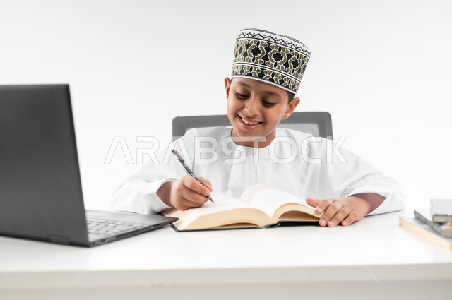 Using modern technical devices, following classes and solving homework online, close-up portrait of an Arab Gulf Omani boy wearing a dishdasha and a kimono reviewing his lessons, studying and distance learning, the concept of e-learning, white background