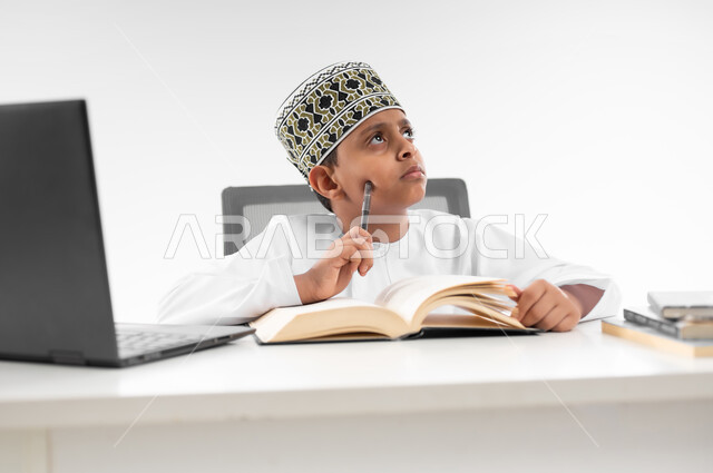 اللهو أثناء الدراسة، استخدام الاجهزة التقنية الحديثة، متابعة الحصص و حل الواجبات عبر الانترنت، بورتريه مقرب لصبي عربي خليجي عماني  يرتدي الدشداشة والكمة ينظر الى الاعلى بايماءات التفكير بشيء ما، مفهوم التعليم الإلكتروني، خلفية بيضاء