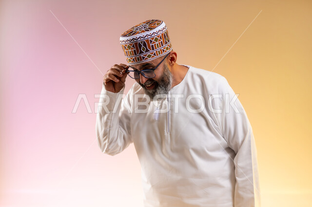 التمعن والتدقيق بشيء ما, مفهوم طول النظر وقصره, بورتريه مقرب لرجل مسن عربي خليجي عماني يرتدي الدشداشه والكمه يمسك النظارة الطبية بإيماءات التركيز، تحسين الرؤية ومحاولة تعديل البصر، خلفية ملونة