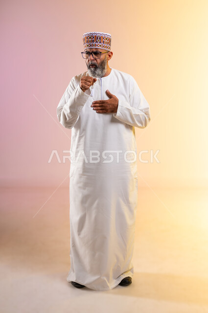 إيماءات الإرهاق والتعب الشديد، الإصابة بالأنفلونزا ونزلات البرد، الكحة والتهاب الحلق والحاجة للعلاج، بورتريه لرجل مسن عربي خليجي عماني يرتدي الدشداشه والكمه يضع يده أمام فمه ويقوم بالسعال, صورة الجسم بالطول الكامل, خلفية ملونة