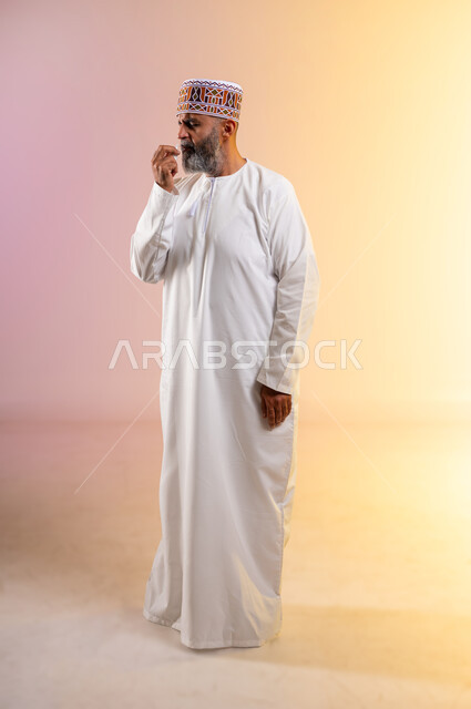 مشاكل في الجهاز التنفسي، بورتريه لرجل مسن عربي خليجي عماني يرتدي الدشداشه والكمه  يحمل بيده جهاز الرذاذ الخاص بمرض الربو، المحافظة على ممر هوائي منتظم, أجهزة استنشاق المخصصة للمرضى، الطولالكامل للجسم، خلفية ملونة