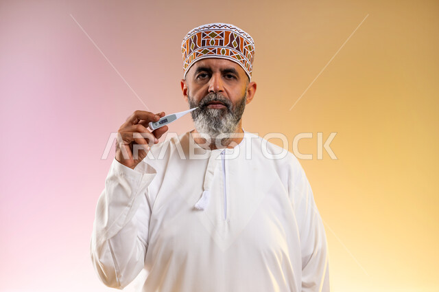 الإحساس بالمرض والإرهاق، بورتريه مقرب لرجل مسن عربي خليجي عماني يرتدي الدشداشه والكمه يقوم بقياس درجة حرارته بإستخدام الميزان الرقمي بتعابير الانزعاج والتعب، ضرورة زيارة الطبيب لوضع الخطة العلاجية، خلفية ملونة