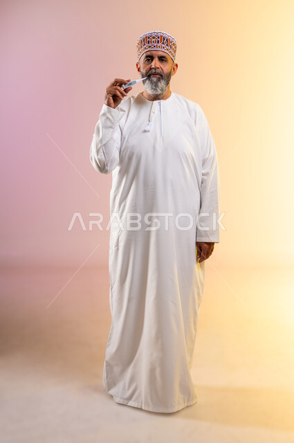 الاصابة بالحمى والتعب, القيام بعرض الميزان الرقمي، ضرورة وجود جهاز مقياس حرارة في المنزل، بورتريه لرجل مسن عربي خليجي عماني يرتدي الدشداشه والكمه ينظر الى الكاميرا بإيماءات الإرهاق بسبب المرض، صورة الجسم بالطول الكامل, خلفية ملونة