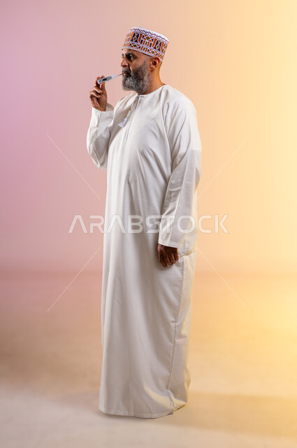 الحاجة إلى زيارة الطبيب للمساعدة ووضع خطة علاجية, الإصابة بالحمى والإرهاق، بورتريه لرجل مسن عربي خليجي عماني يرتدي الدشداشه والكمه يقوم بقياس حرارته باستخدام الميزان الرقمي، إيماءات التعب بسبب المرض, الطول الكامل للجسم، خلفية ملونة