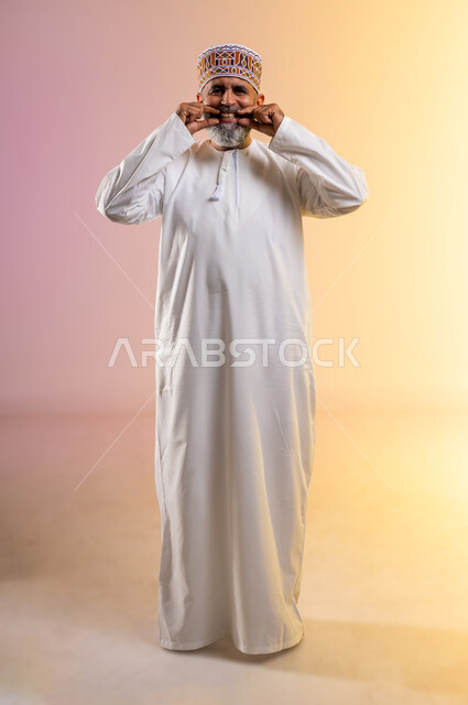 استخدام قشور فينير من الخزف لصنع ابتسامة بيضاء ناصعه، أهمية متابعة طبيب الاسنان، العناية والتجميل والتبيض، بورتريه لرجل مسن عربي خليجي عماني يرتدي الدشداشه والكمه يشير بيديه إلى أسنانه, النظرإلى الكاميرا بإيماءات السعادة، الطول الكامل للجسم، خلفية ملونة