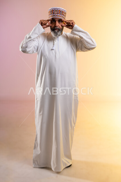 مشاكل عينيه وحالات مرضية، الحاجة للفحص والعلاج، التهاب القرنية العينية،  ارتفاع ضغط العين، بورتريه لرجل مسن عربي خليجي عماني يرتدي الدشداشه والكمه يقوم بفتح عينيه باستخدام يديه، احمرار و وجع العيون، الطول الكامل للجسم، خلفية ملونة