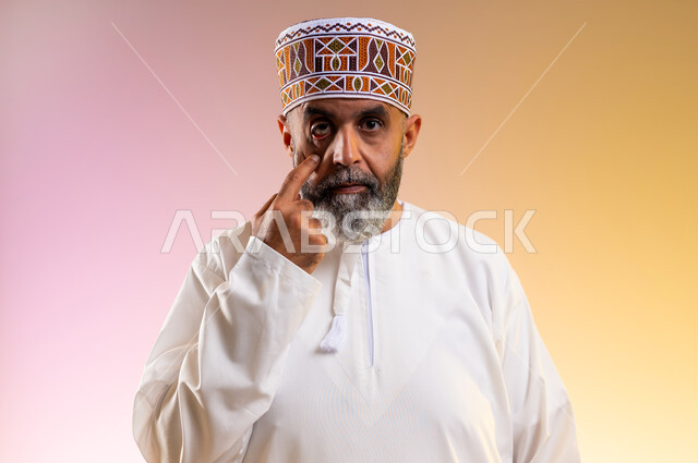 التهاب القرنية العينية، ارتفاع ضغط العين، بورتريه مقرب لرجل مسن عربي خليجي عماني يرتدي الدشداشه والكمه يقوم بفتح عينه باستخدام اصبع السبابة، احمرار و وجع العيون، مشاكل عينيه وحالات مرضية، الحاجة للفحص والعلاج، خلفية ملونة