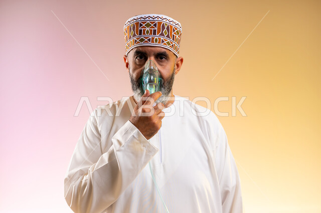المحافظة على ممر هوائي منتظم باستخدام جهاز التنفس الصناعي، بورتريه مقرب لرجل مسن عربي خليجي عماني يرتدي الدشداشة والكمه يقوم باستنشاق أدوية معالجة لانقطاع التنفس عن طريق قناع الاكسجين، تقديم الخدمات الصحية المنزلية، مداواة أمراض الربو المزمنة، خلفية ملونة