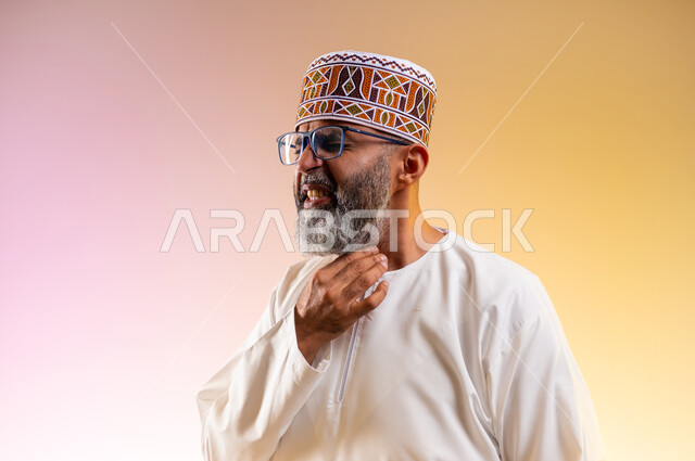 الاحساس بألم البلعوم, الحاجة إلى العلاج والدواء, مفهوم الاهتمام بالصحة, الاصابة بنزلة برد والتهاب الحلق، بورتريه مقرب لرجل كبير بالسن عربي خليجي عماني يرتدي الدشداشه والكمه يضع يديه على حلقه ويشعر بالاختناق, خلفية ملونة