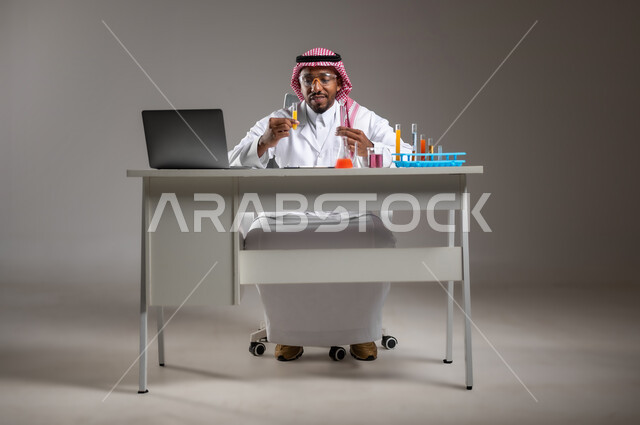 إيماءات الدقة والتركيز، إجراء التفاعلات الكيميائية, اكتساب المعرفة والخبرة، الدراسات والتجارب في بيئة عملية متطورة, بورتريه لرجل عربي خليجي سعودي يرتدي الزي التقليدي و نظارة الوقاية يجلس امام الحاسوب المحمول يقوم بتجربة علمية, صورة لكامل الجسم، خلفية رمادية