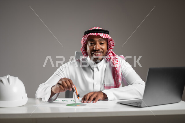 Engineering project management, gestures of joy and happiness, integrating technology into work, studying project basics, working in engineering sector, close-up portrait of a Saudi Arabian Gulf engineer wearing traditional thobe sitting at desk checking and reviewing construction plans, gray background