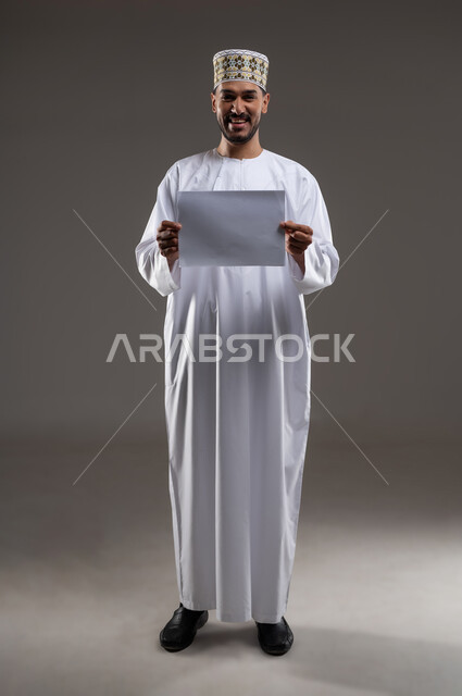 القراءه والمطالعه ودراسه المشاريع، بورتريه لرجل عربي خليجي عماني يرتدي الدشداشه والكمه يقوم بتصفح أوراقا بيضاء، قضاء أوقات الفراغ في التثقيف والتعليم، مفهوم التعليم الذاتي وممارسة الهوايات الممتعة والمفيدة في المنزل, خلفية رماديه