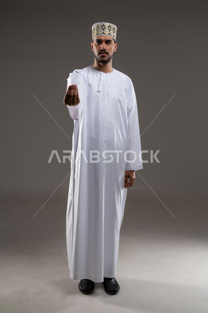 حركة يد تعني خفض الصوت والهدوء، ايماءات وجه ويدين تدل على محاولة تهدئة نقاش حاد، بورتريه لرجل عربي عماني يرتدي الدشداشة والكمه تظهر عليه علامات الانزعاج وعدم الراحة، طريقة الطلب بأدب واحترام، خلفية رماديه
