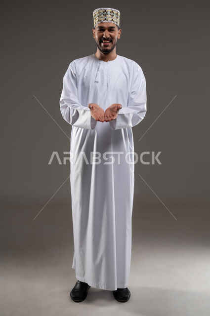 حركة يد تدل على طلب العون والمساعدة، مد الكفين للإمام اشارةً للحاجة، بورتريه لرجل عربي خليجي عماني يرتدي الدشداشة والكمه يمد يديه للامام طلبا للمساعده ايماءات عجز وترجي، خلفية رماديه