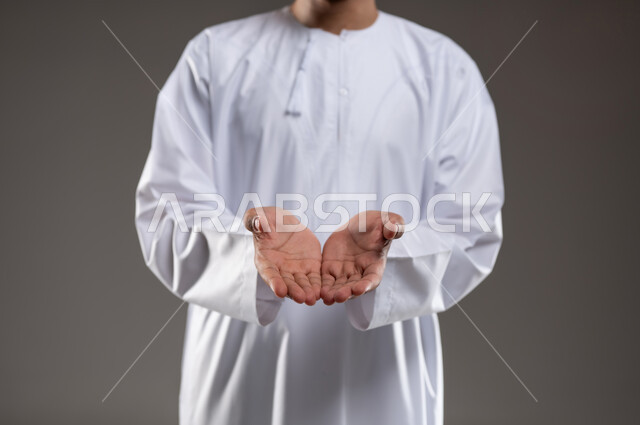 حركة يد تدل على طلب العون والمساعدة، مد الكفين للإمام اشارةً للحاجة، بورتريه لرجل عربي خليجي عماني يرتدي الدشداشة والكمه يمد يديه للامام طلبا للمساعده ايماءات عجز وترجي، خلفية رماديه
